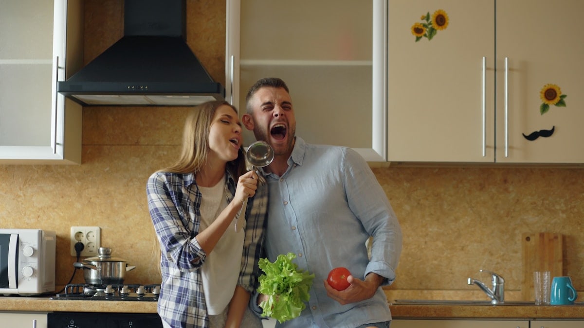 Attractive young joyful couple have fun dancing and singing while cooking in the kitchen at home in the morining
