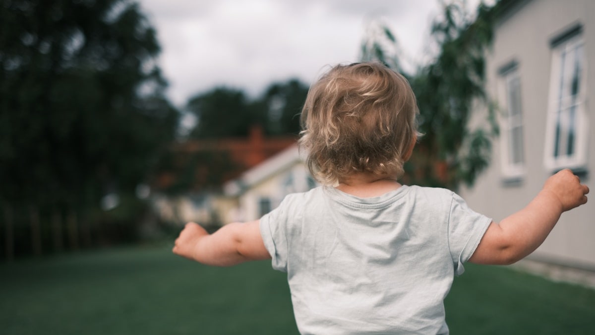 A little boy standing in the grass with his arms outstretched